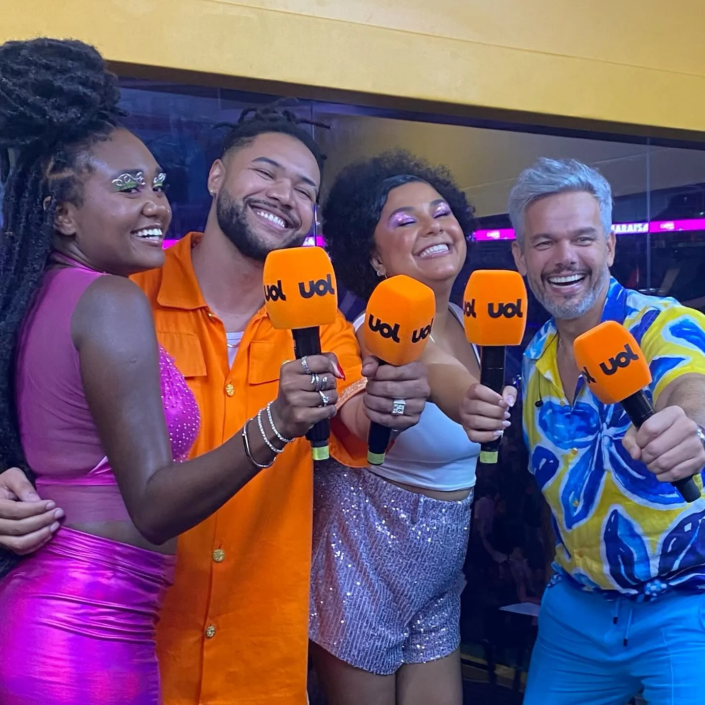 Arape Malik de macacão laranja com microfone da UOL, ao lado de outros apresentadores