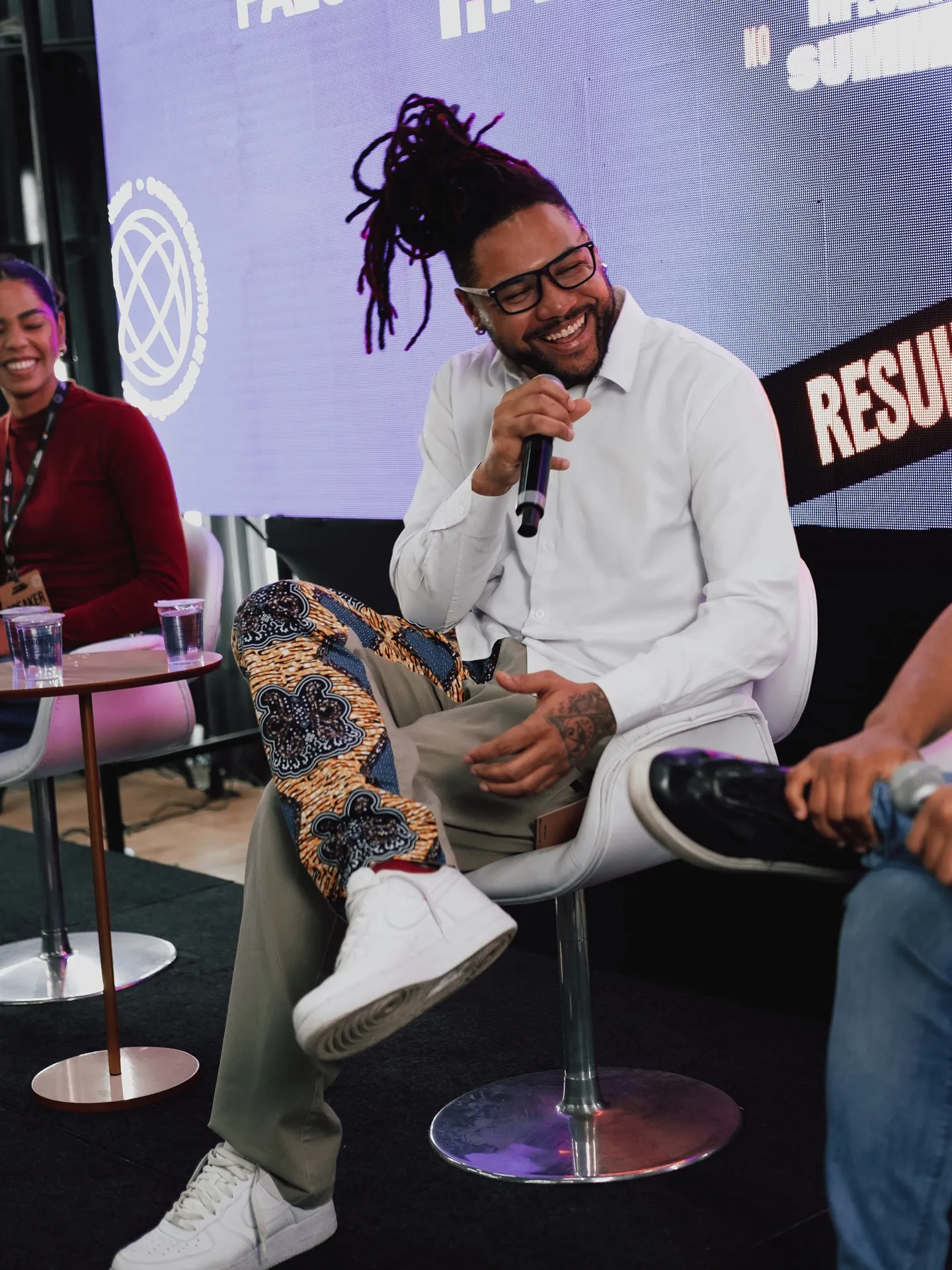 Arape Malik sentado no palco do Influent Summit, de microfone na mão