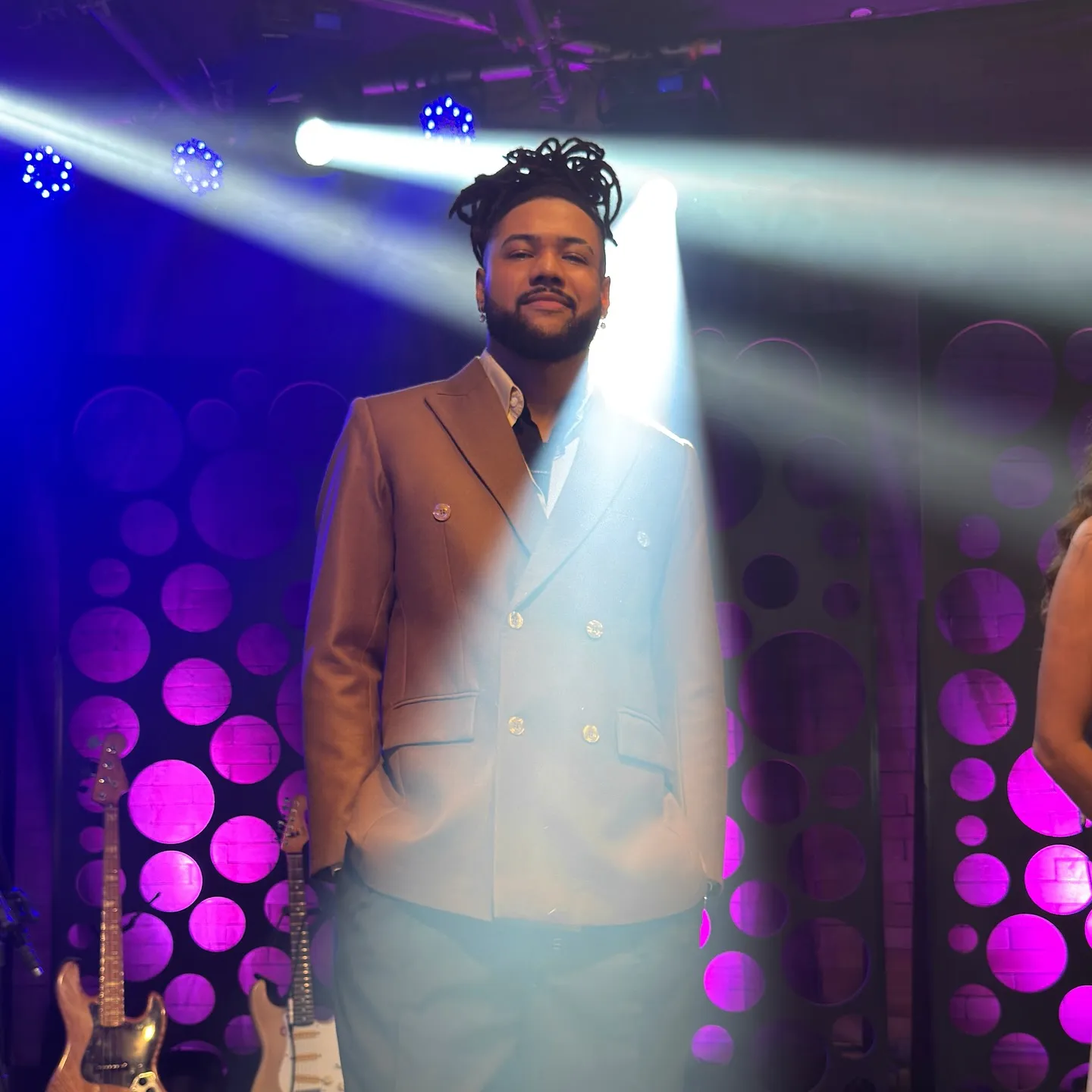 Arape Malik de terno, sob o foco de luz no palco do Toca Revela